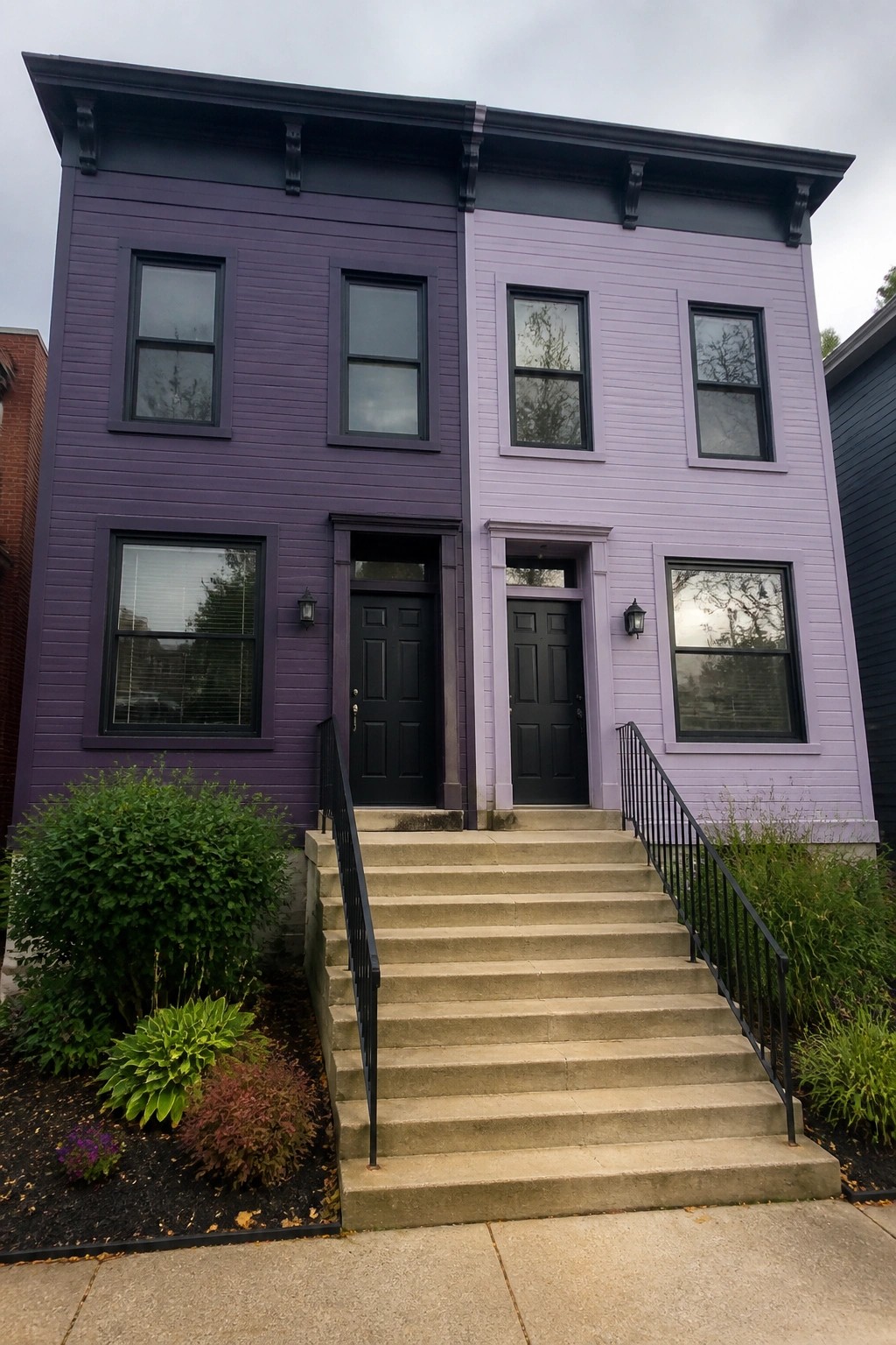 A two-story house with smooth siding split into dark purple on the left half and light purple on the right half, black windows and doors, and concrete steps leading to two separate entrances.