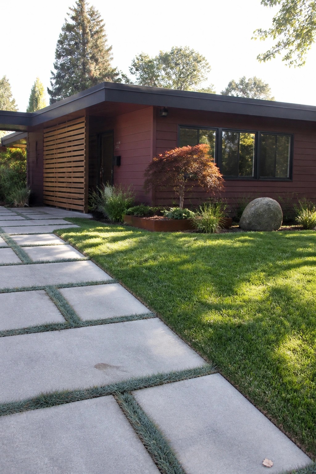 Modern red house with concrete pavers on grass, large windows and landscaping