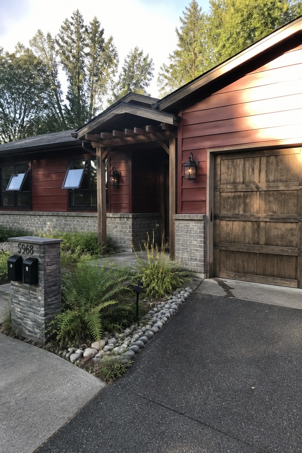A single-story house with burgundy horizontal lap siding, a wooden garage door, stone foundation accents, and a covered entry with wood beams.