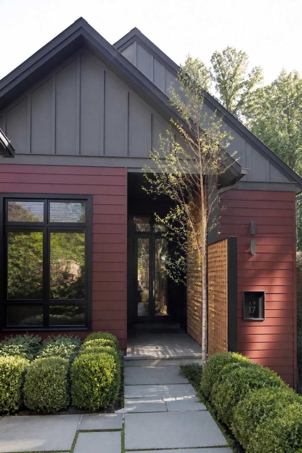 A modern house exterior with burgundy horizontal lap siding on the lower walls, gray siding above, a large black-framed window, and a glass front door.