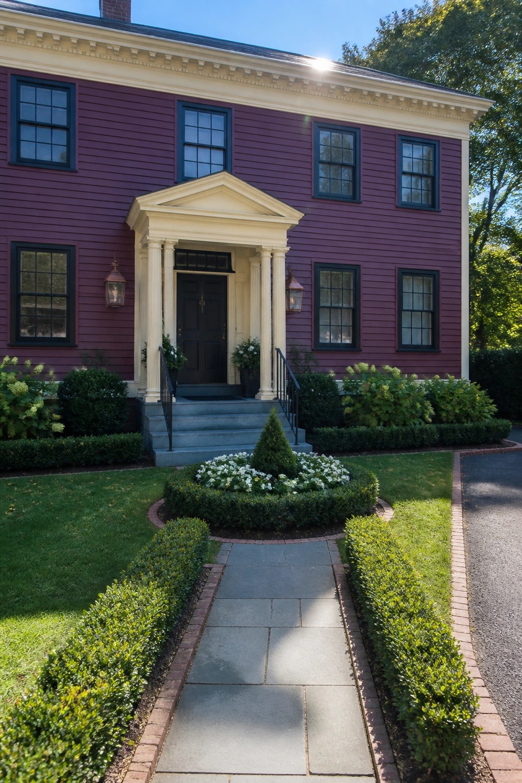 Maroon house with white portico, dark door, stone path, and blooming garden