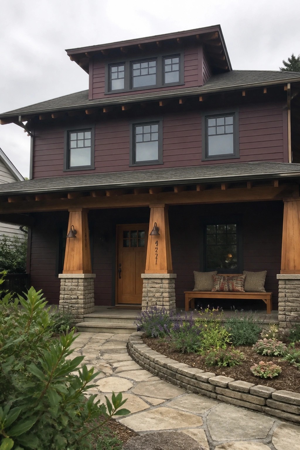 Two-story maroon house with wooden porch, stone pillars, bench, and stone pathway.