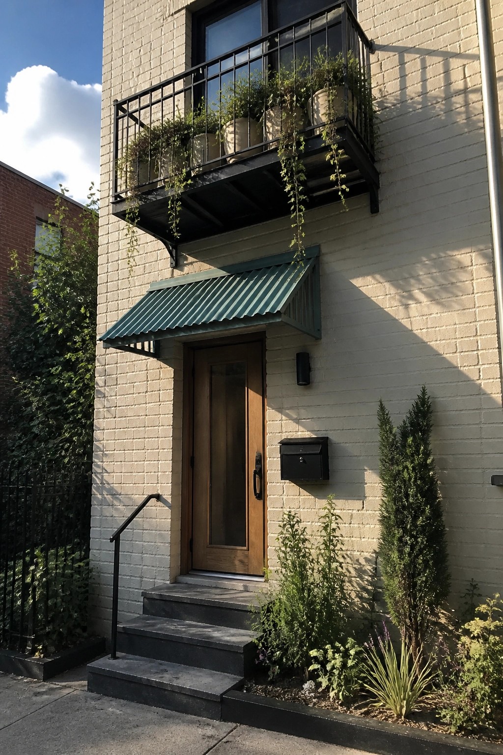 White brick building entrance with wooden door, green awning, and plant-filled balcony.