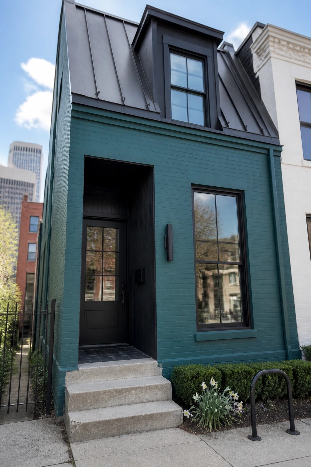 Front view of a narrow teal brick house with a black metal roof, black door, and black window frames, concrete steps at the entrance.