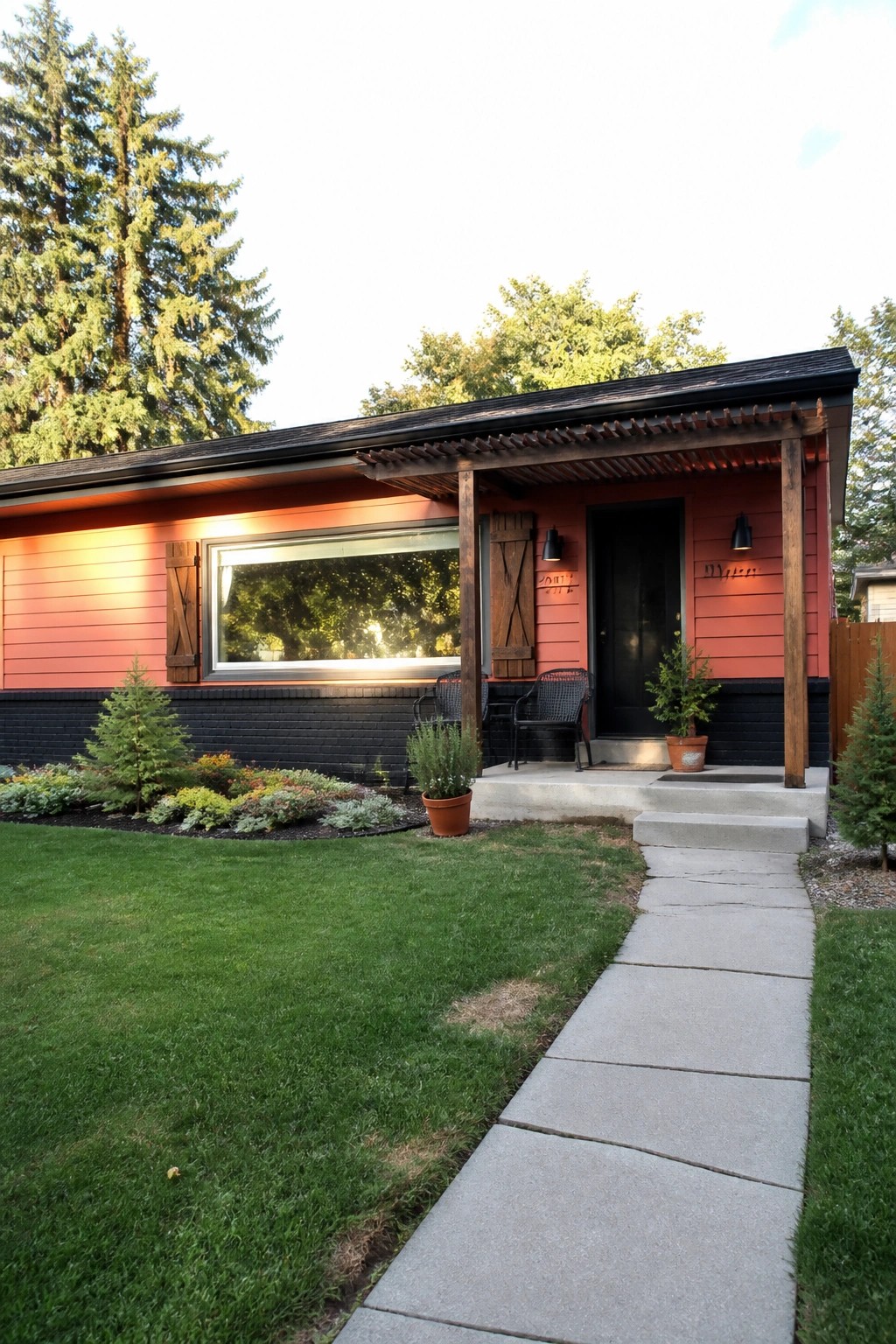 Red ranch house with covered porch, black door, concrete walkway, and green lawn.