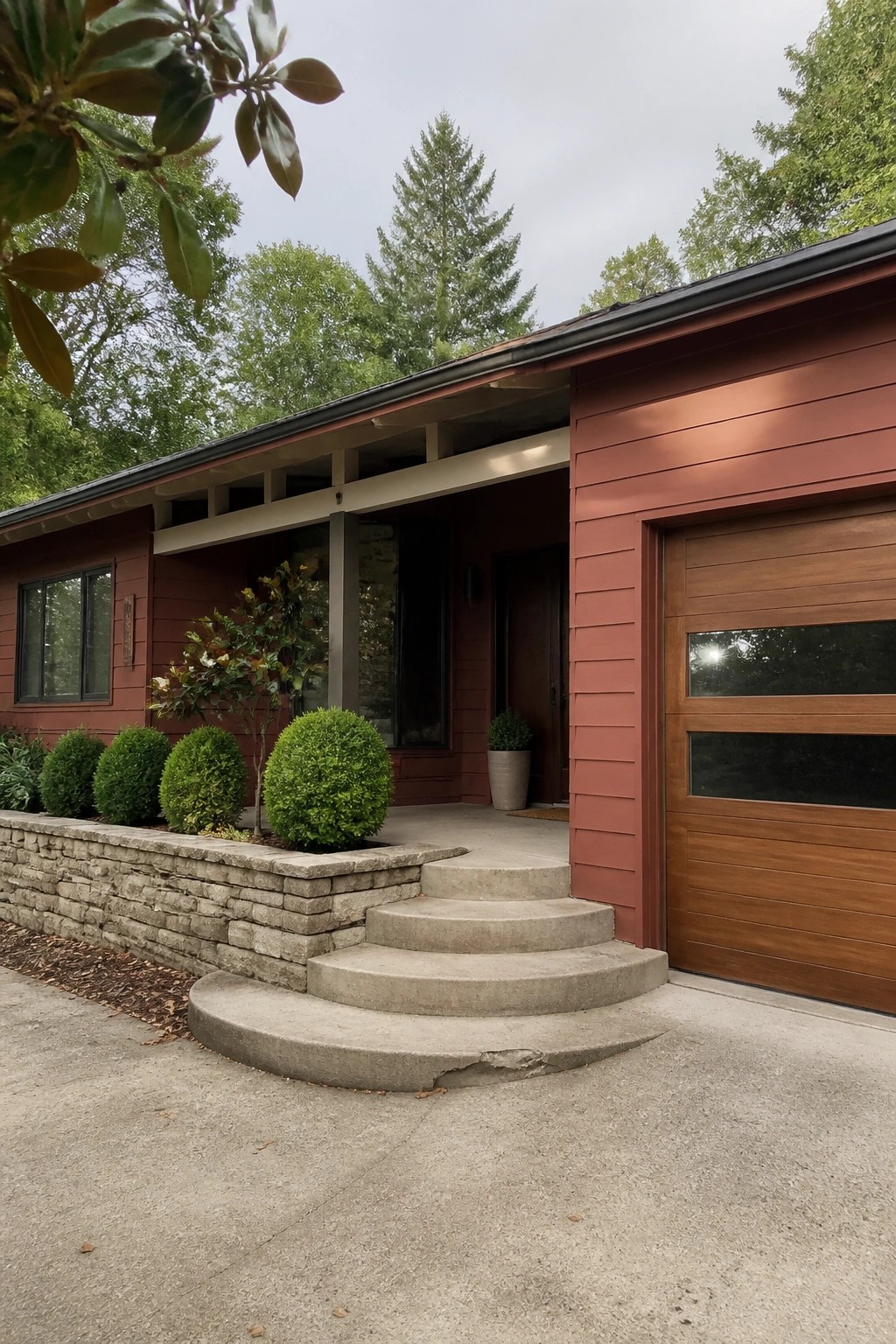 Red modern house with wooden garage door, concrete steps, and stone retaining wall.