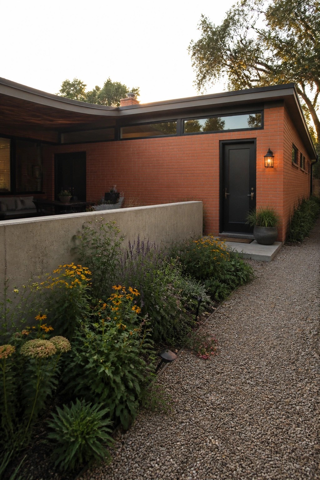 Modern red brick house with black door, flower garden, and gravel path.