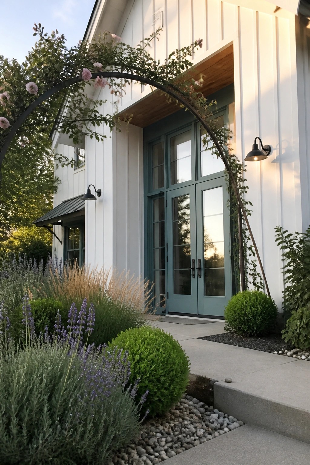 A white board-and-batten house exterior with light teal double doors beneath a wooden overhang and an arched metal arbor with climbing roses.