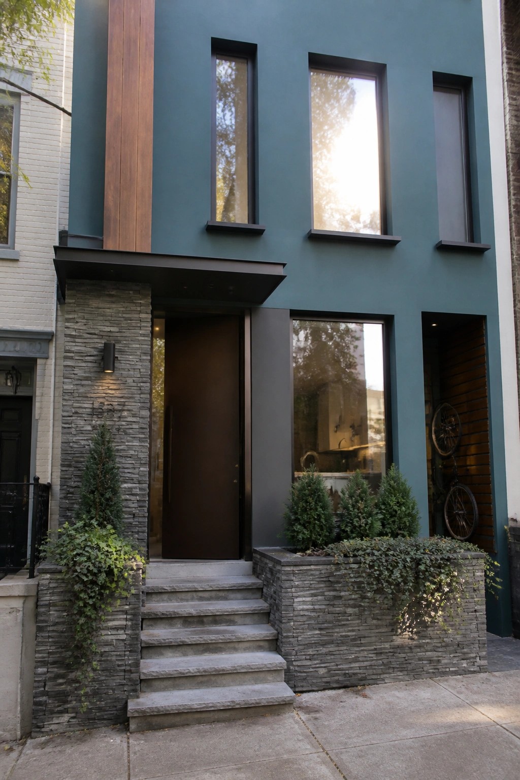 Modern teal house with brown door, stone steps, windows, and bicycles.