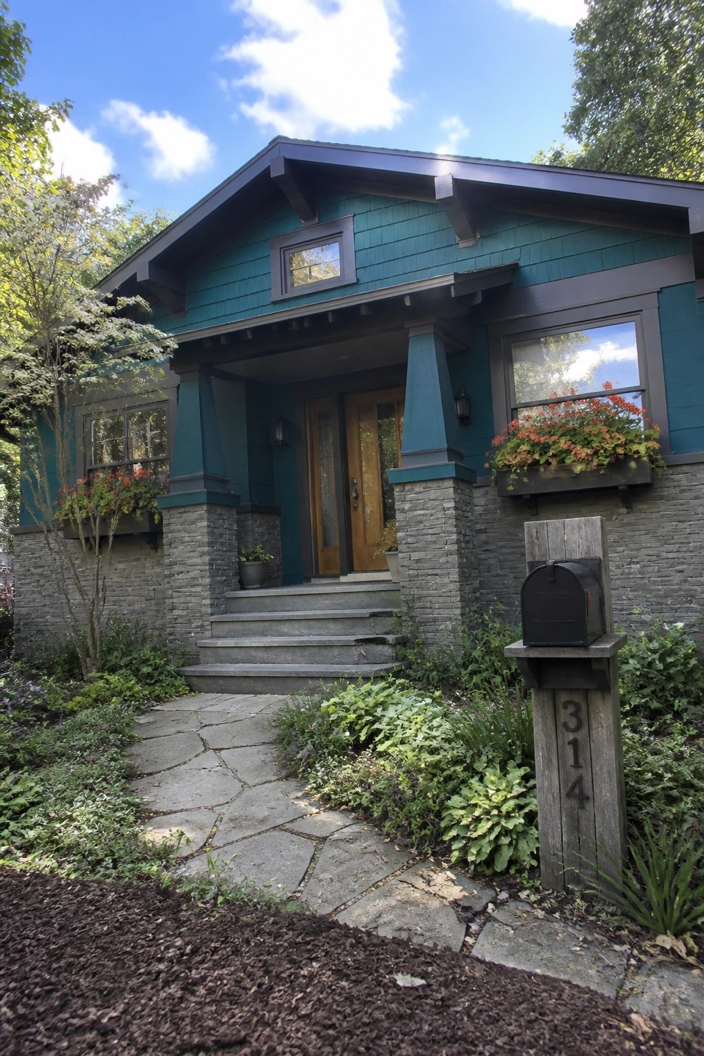 A teal house exterior with gray stone veneer on the lower walls and porch columns, a wooden front door, stone steps, and a stone pathway.