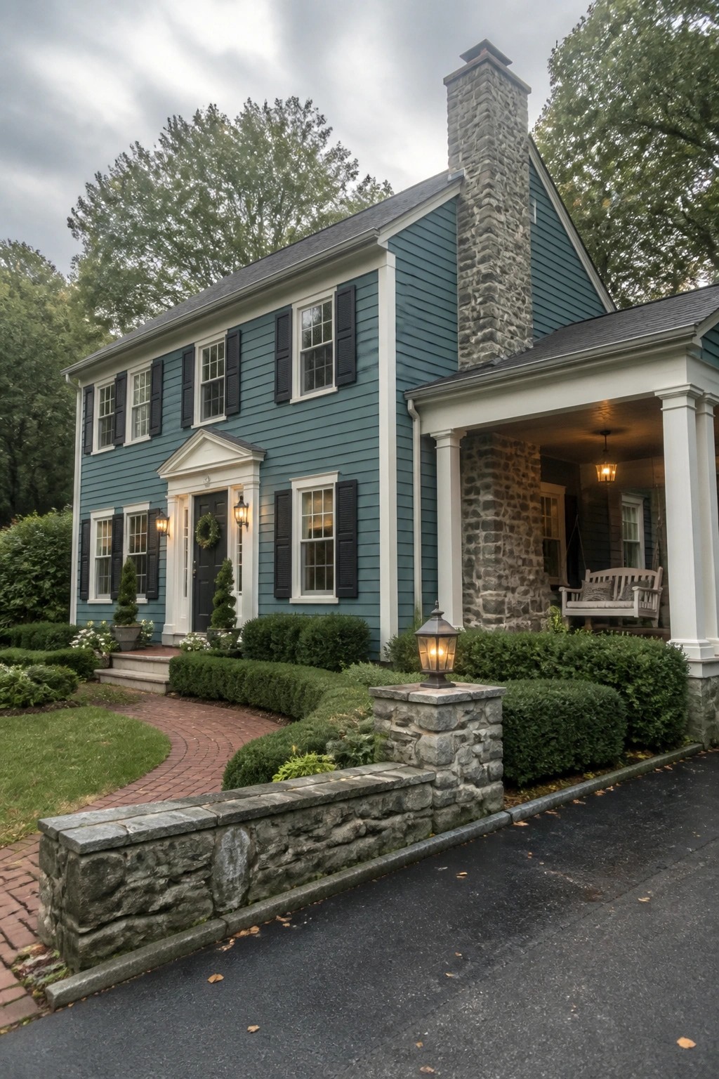 A two-story teal house with white trim, black shutters, a large stone chimney, and a front porch supported by white columns.