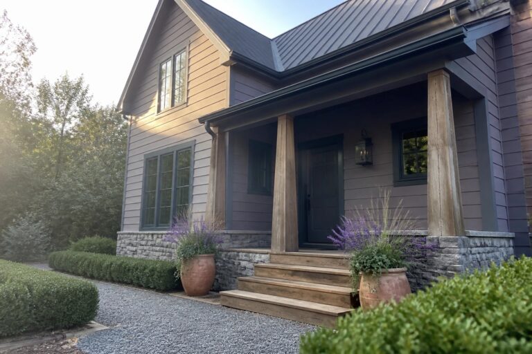 21 Refined Purple Gray House Exteriors Featuring Charcoal Accents A house with purple-gray siding, charcoal roof and trim, black double doors under a porch supported by wooden posts, and large terracotta pots beside the steps.