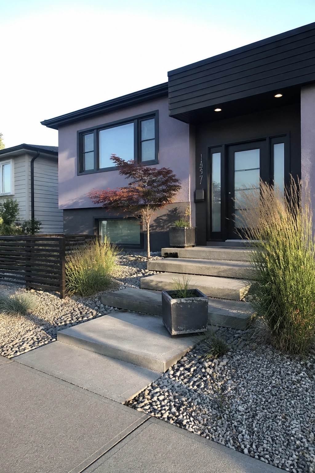 A modern house with purple-gray siding, black door and window frames, concrete steps, and gravel landscaping around the entry.