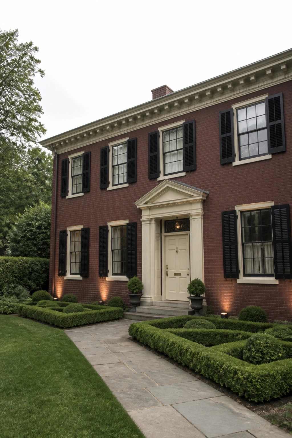 A two-story red brick house with cream trim, black shutters, and a white door framed by a classical pediment.