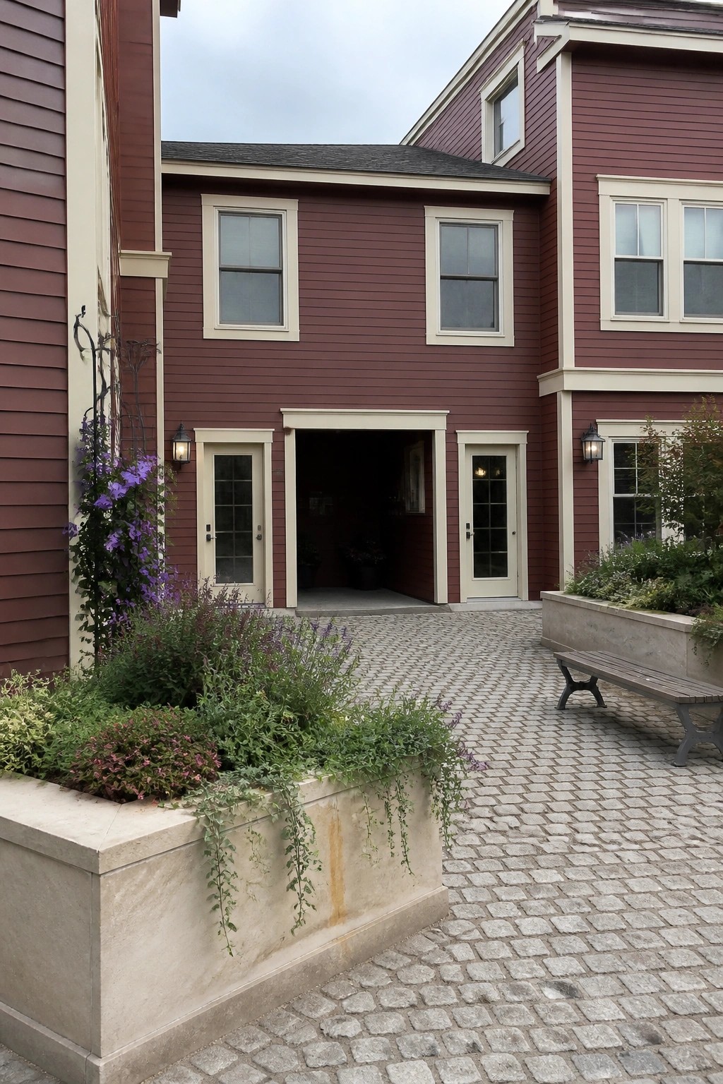 A two-story house exterior with wine red siding, cream trim around windows and doors, and an open central doorway flanked by smaller cream doors on a cobblestone surface.