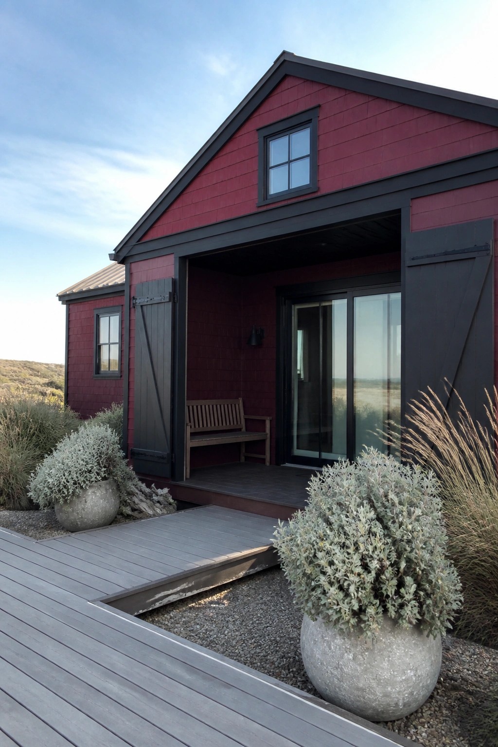 Red barn-style house with black trim, porch bench, and potted plants on deck.