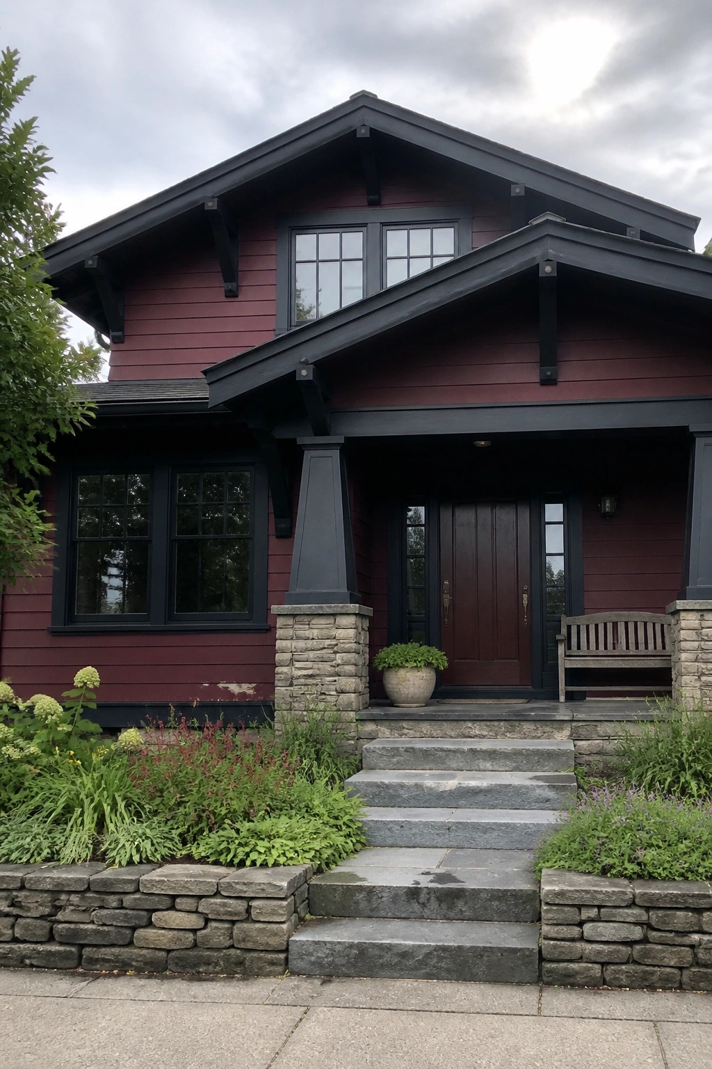 A two-story house with burgundy siding, black trim around windows and roof edges, a stone porch, and gray steps leading to a dark front door.