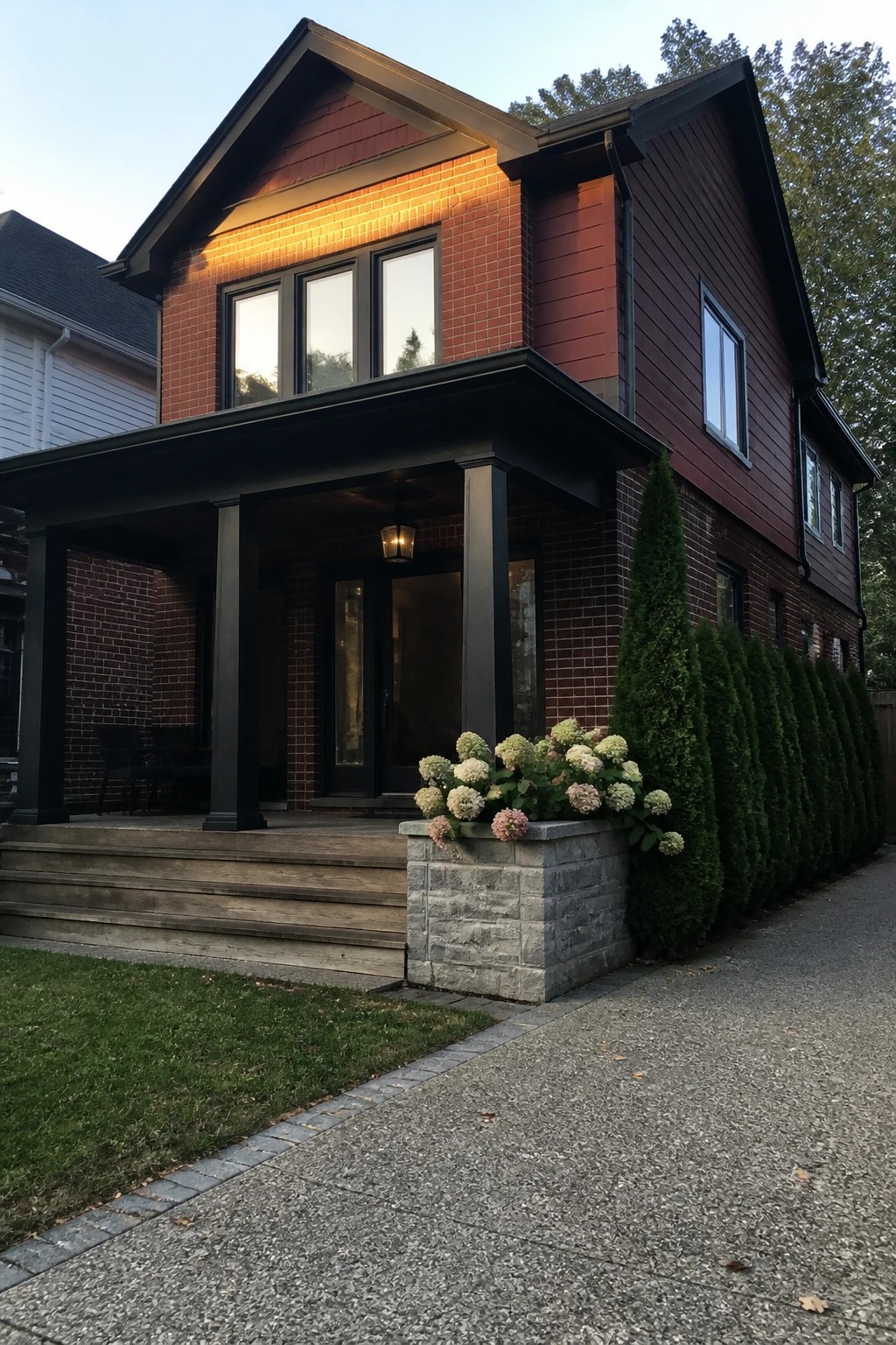 Two-story red brick house with dark siding, black porch, wooden steps, and flower planter.