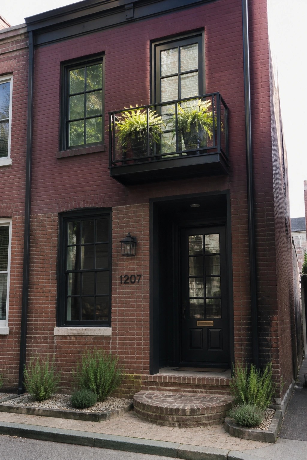 Red brick building with black door 1207, balcony, windows, and shrubs.