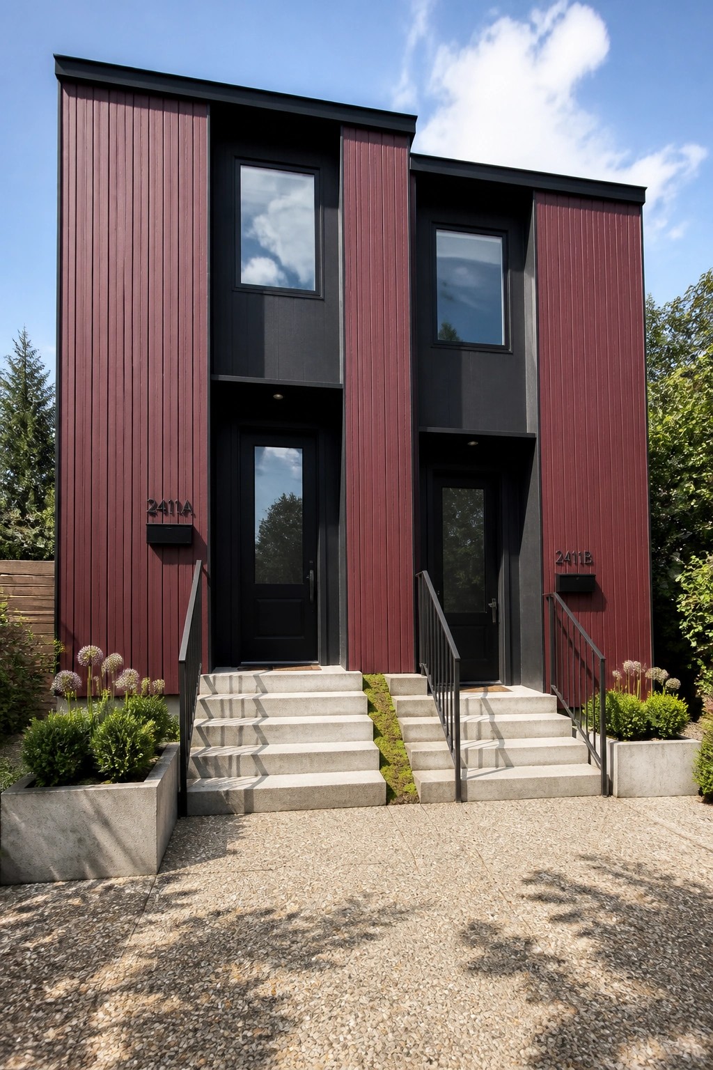 A two-story duplex with vertical burgundy siding, black window and door frames, and two black entry doors with concrete steps leading up to each.