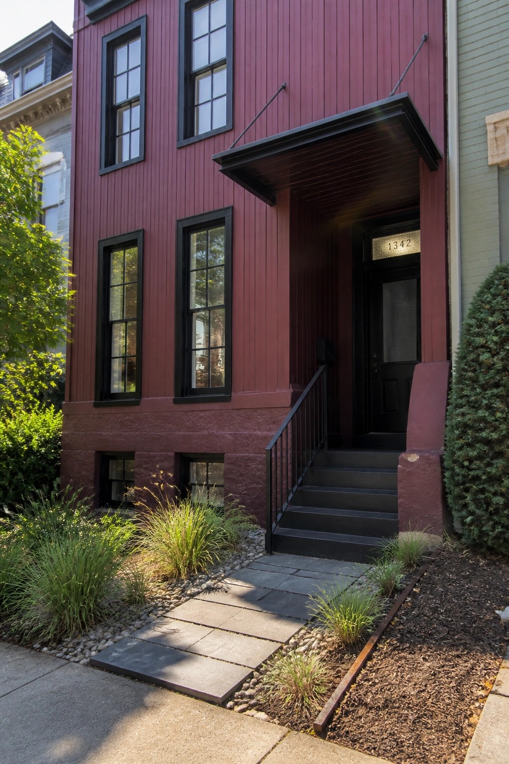 Maroon wooden townhouse with black door 1342, steps, railing, and garden path.