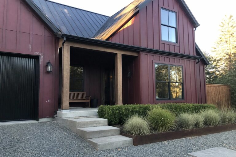 Modern dark red house with black trim, wooden porch bench, and gravel driveway.