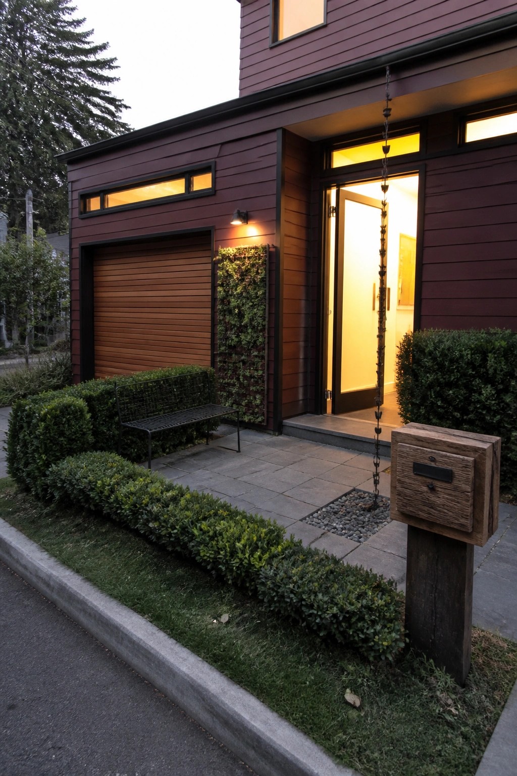 Modern maroon house with open lit door, vertical garden, bench and wooden mailbox.