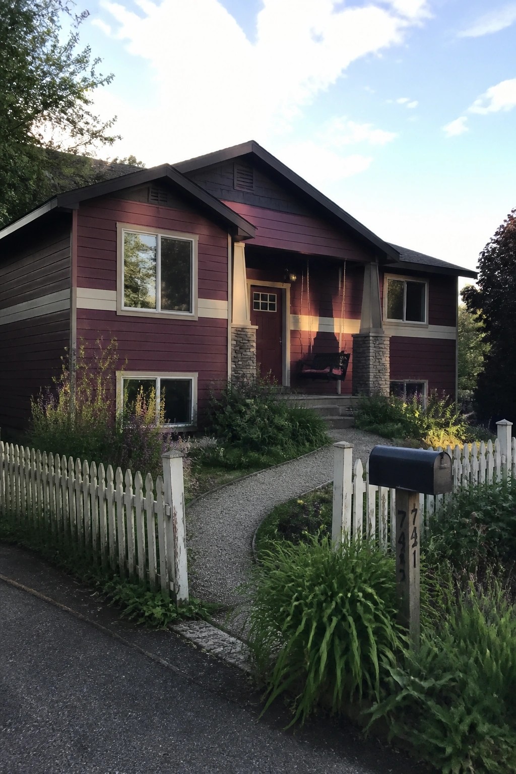 Maroon two-story house with porch swing, gravel path, white fence, and mailbox.
