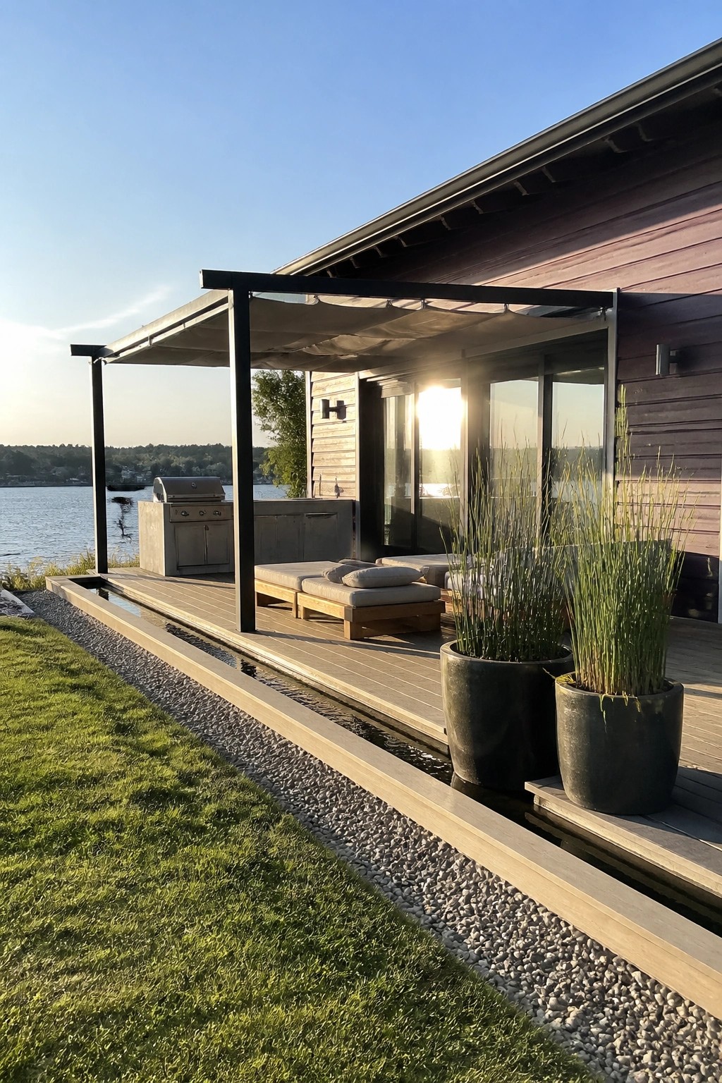 Modern waterfront deck with lounge chairs, grill, pergola, and potted plants at sunset