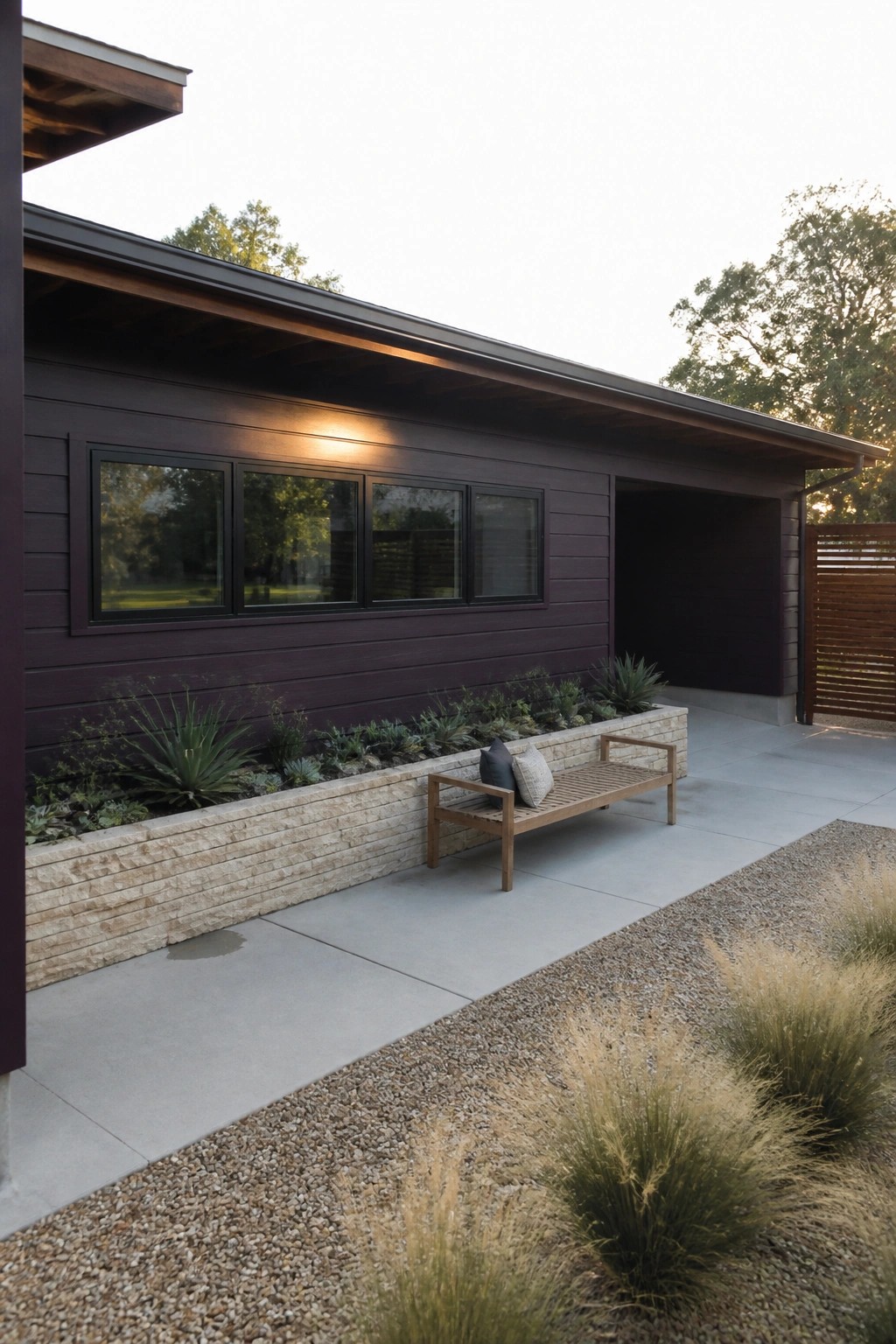 Modern dark house with windows, wooden bench, stone planter, and gravel garden at dusk