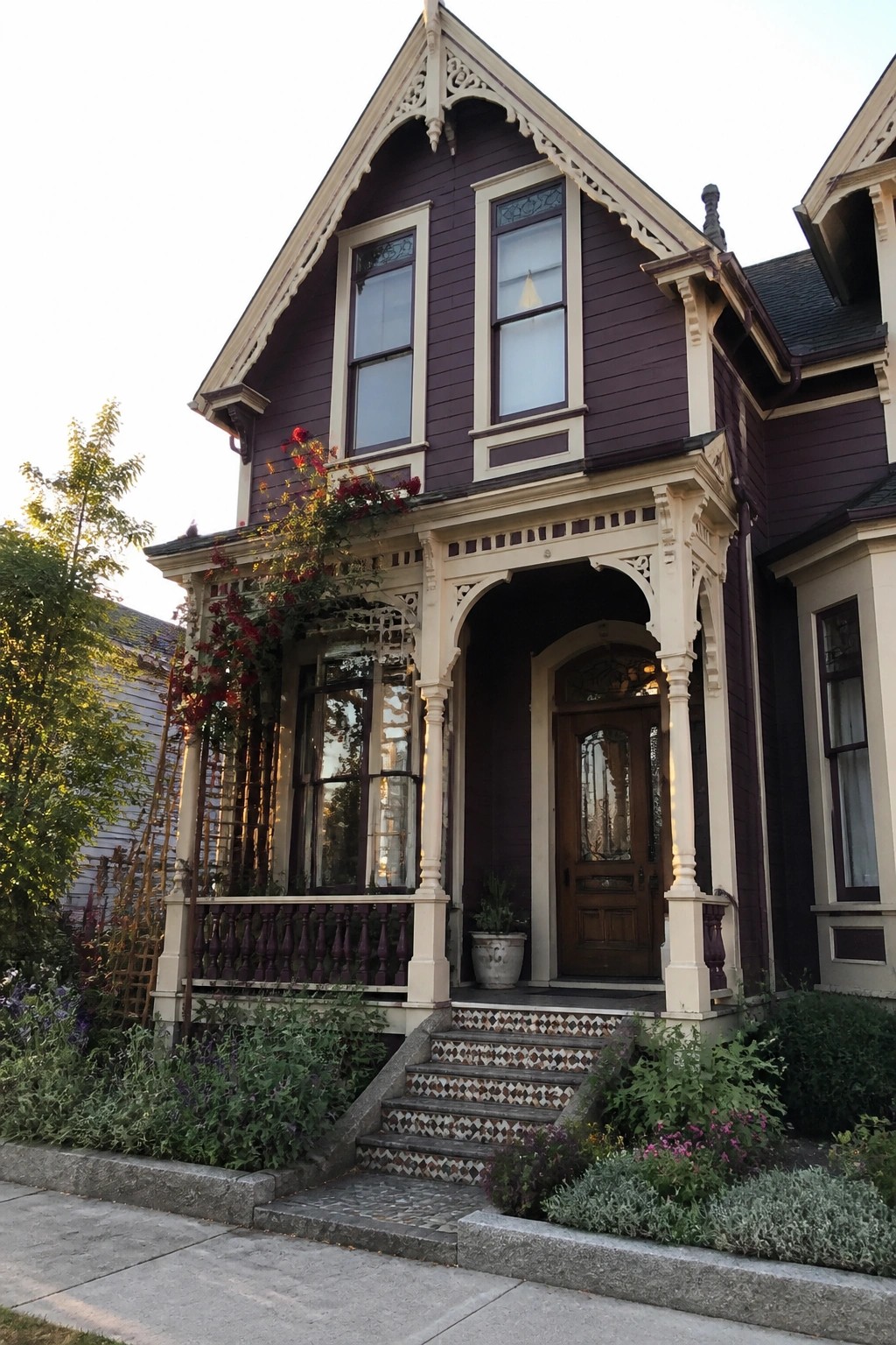 Purple Victorian house with cream trim, arched porch, mosaic steps, and red flowers.