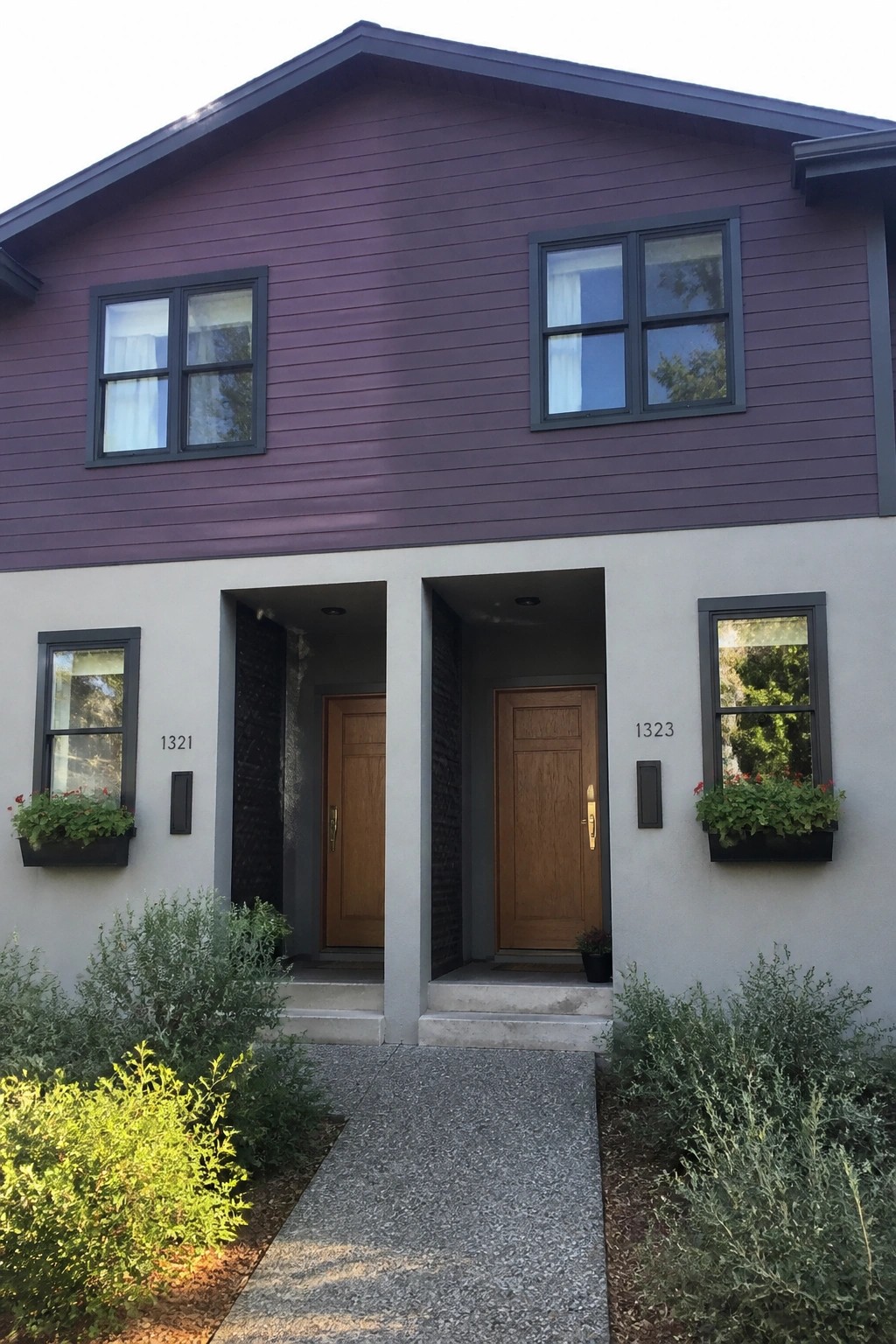Purple duplex with two wooden doors, windows, and flower boxes with plants.