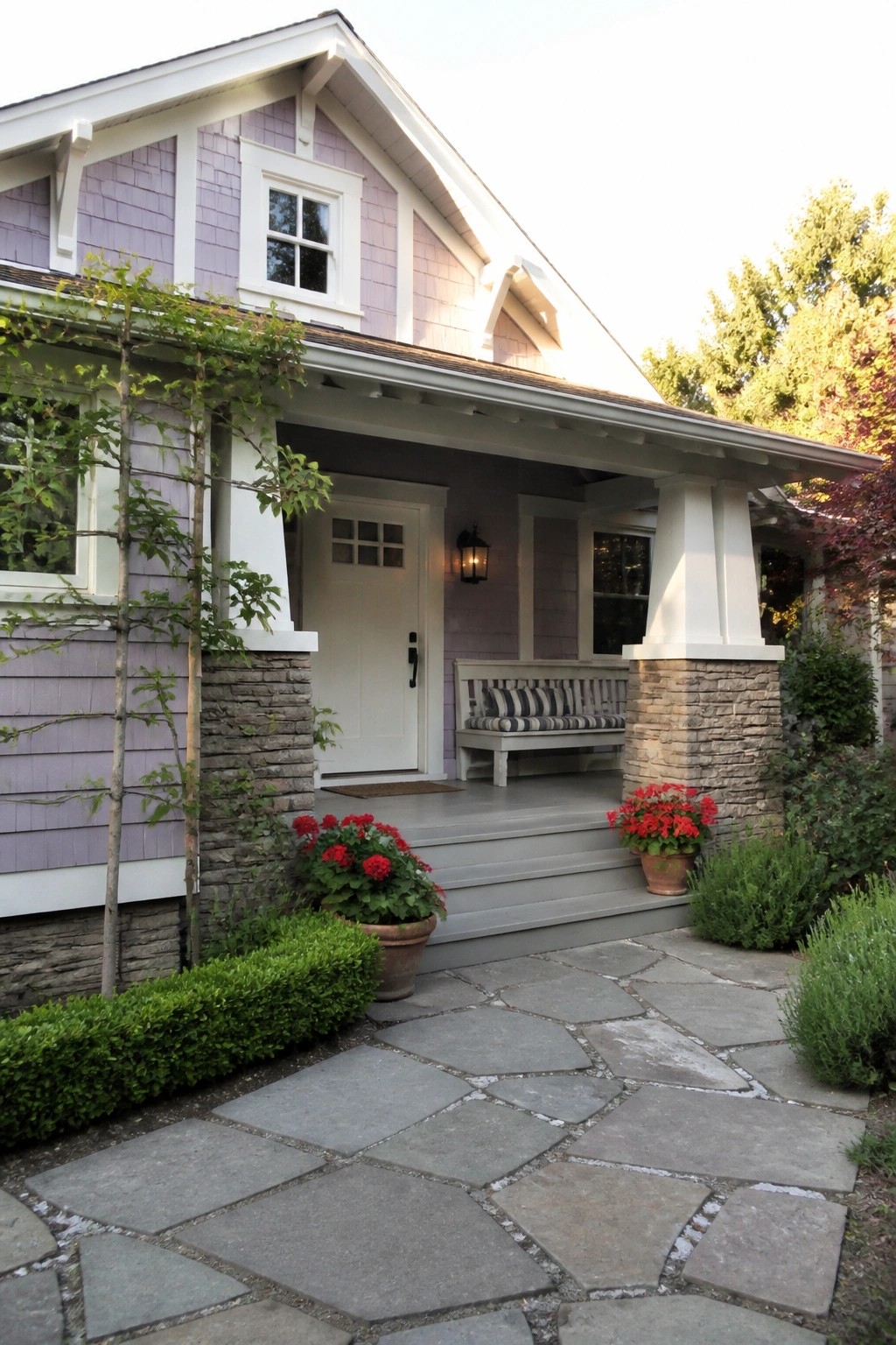 Purple house with white porch, stone pillars, red flowers, and stone path.