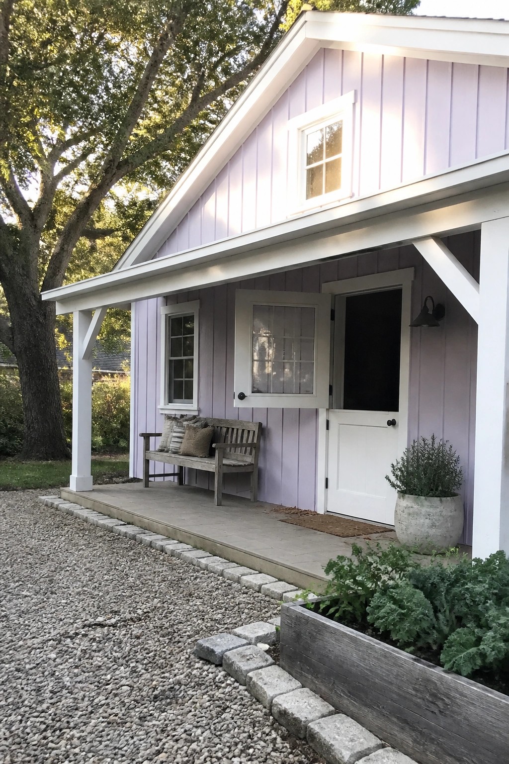 Lavender cottage with white trim, wooden porch bench, open door, and garden bed.
