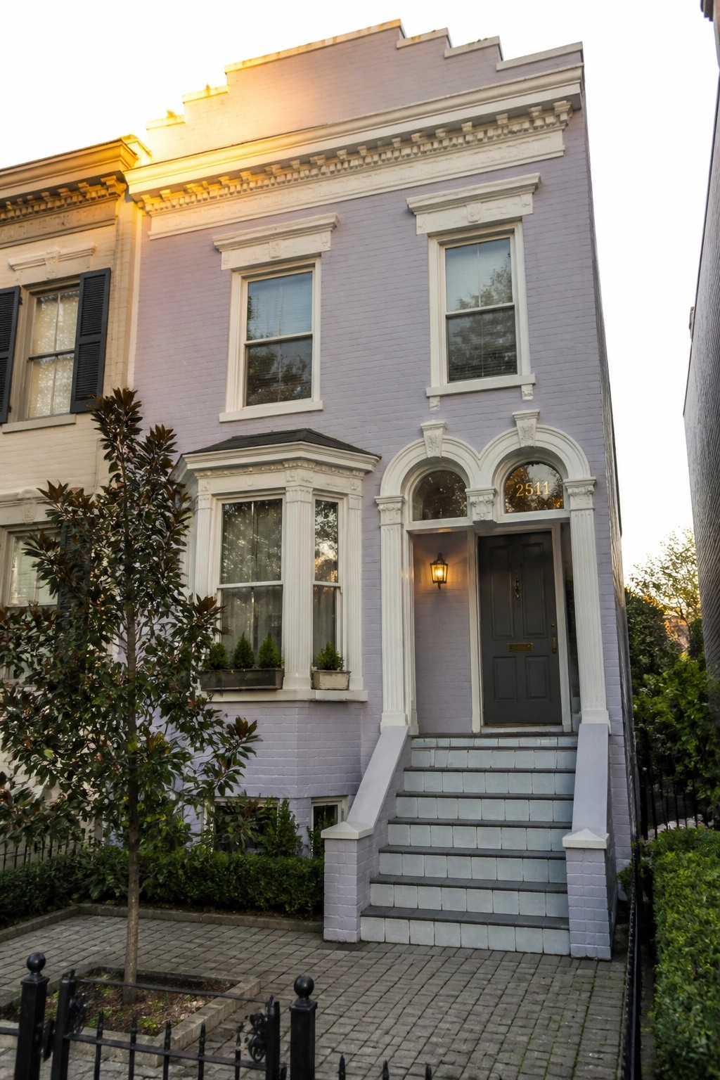 A lilac brick house with white trim around the windows, arched doorways, and cornice, shown from the front with steps leading to the door.