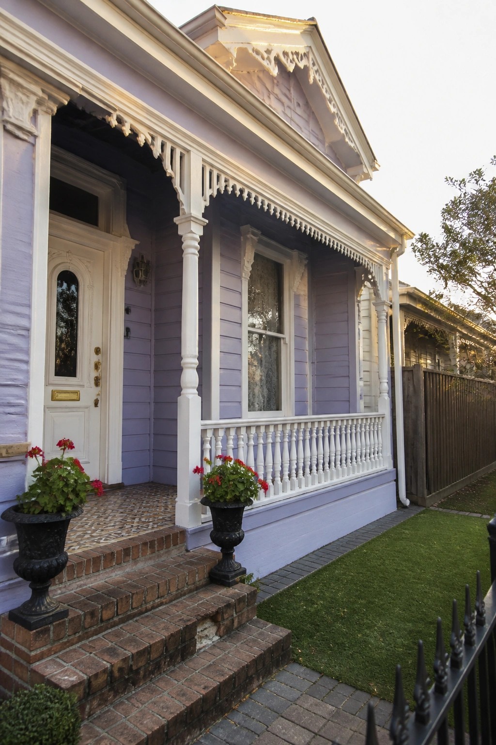 A lilac house with white trim shows a front porch, columns, railings, and brick steps with potted plants.