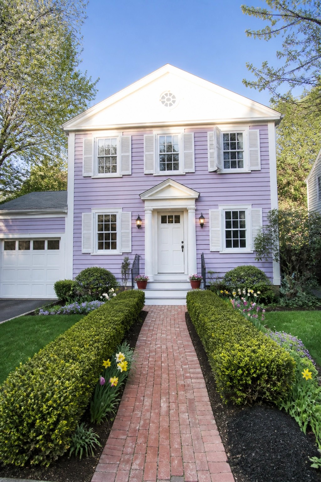A two-story house with lilac siding, white trim around the windows and door, white shutters, and a brick path leading to the front steps.