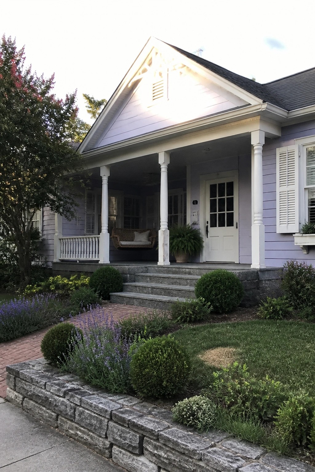 Front view of a light purple house with white trim, porch columns, white door, and stone steps, with landscaping in the foreground.