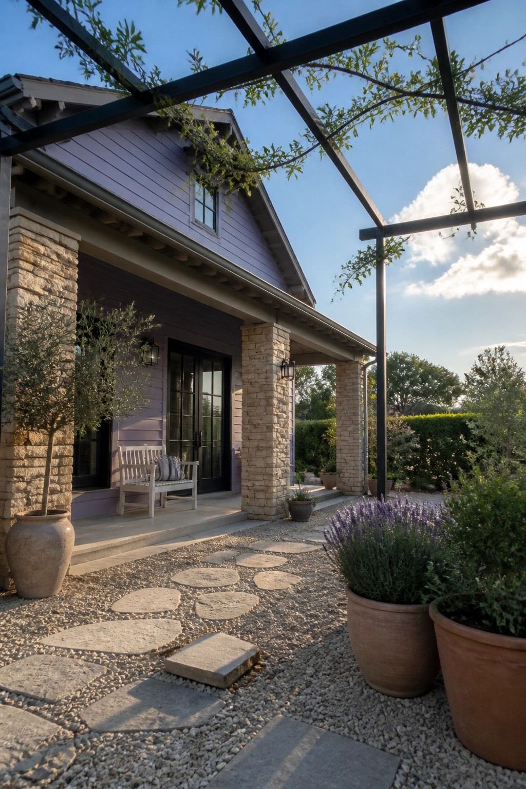 Purple house with stone pillars, white bench, gravel path and potted lavender under pergola.
