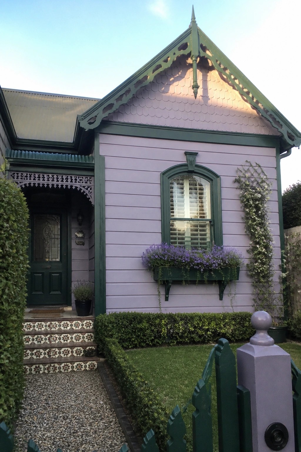 Light purple house with green trim, flower box, ivy, and garden path