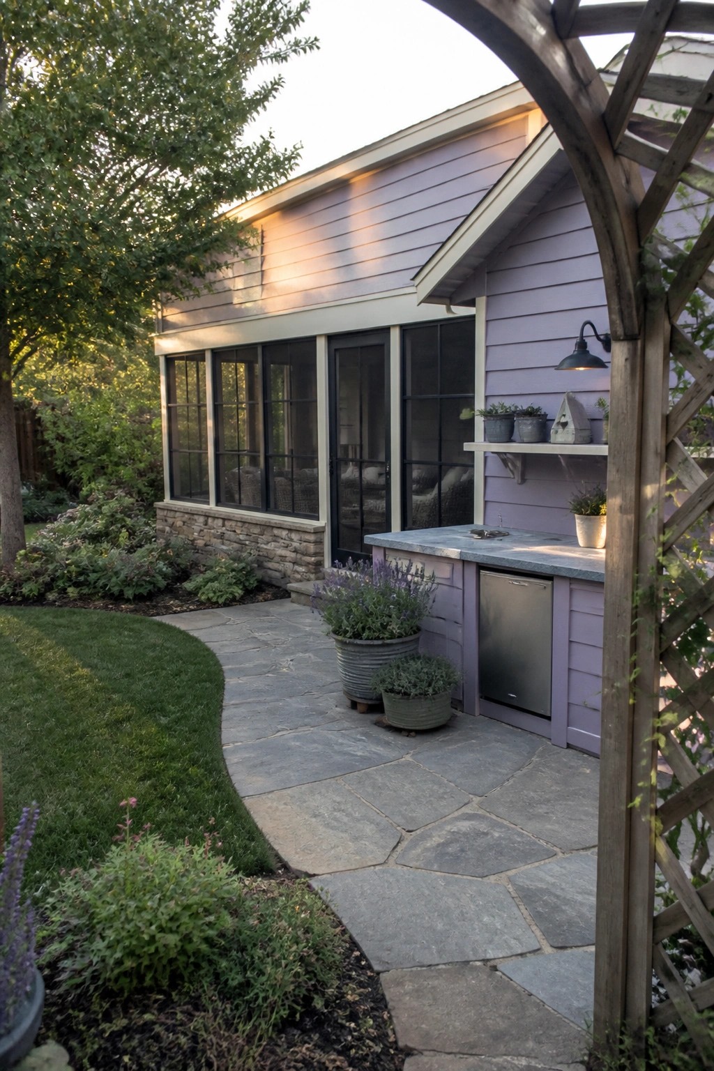 Purple house with outdoor kitchen on stone patio amid garden path and plants.