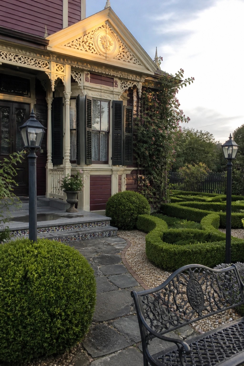 A burgundy Victorian house exterior with ornate cream trim, black shutters, a stone path, and trimmed shrubs in the garden.