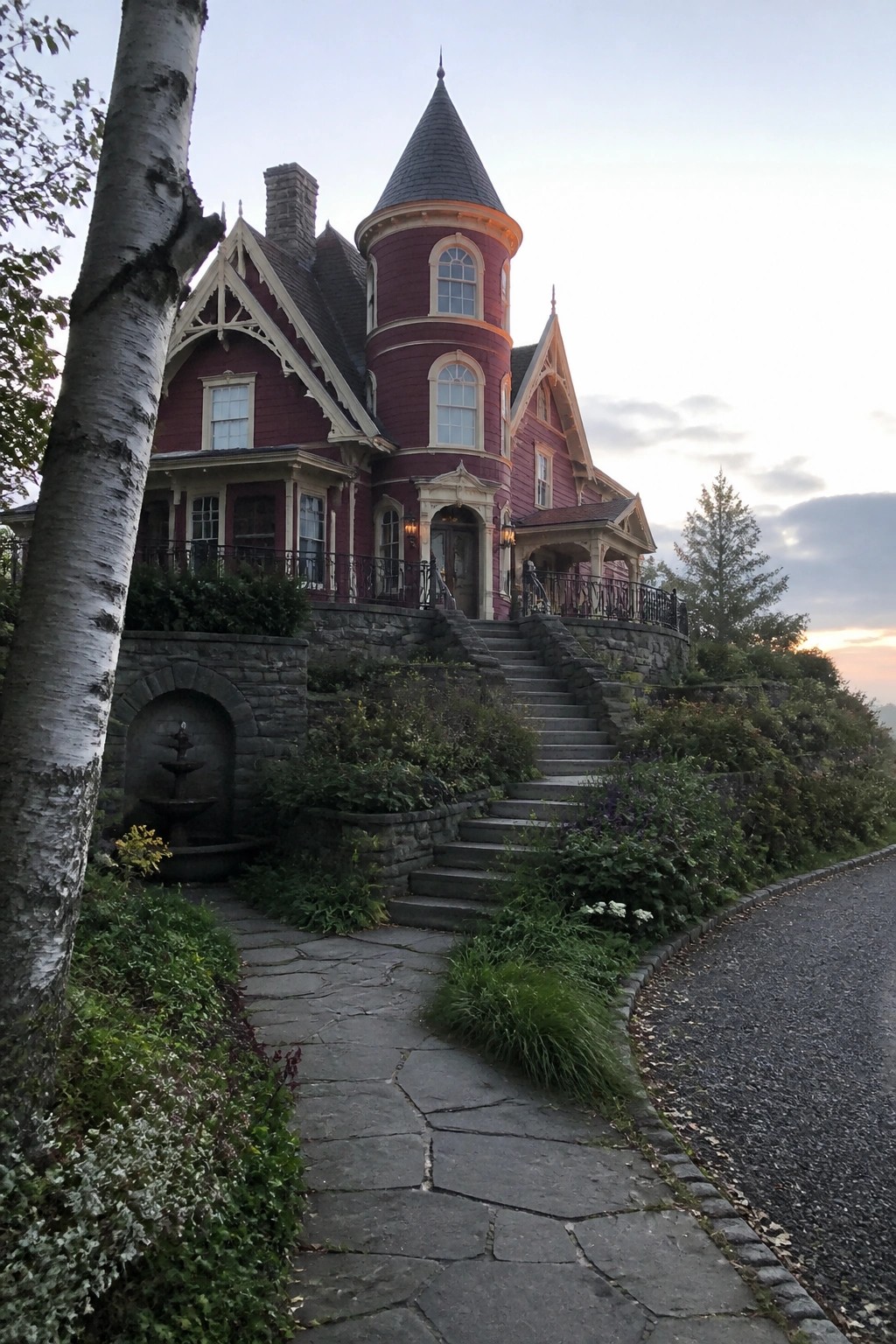 A burgundy Victorian house with cream trim, a round tower, and stone steps leading to the front entrance.