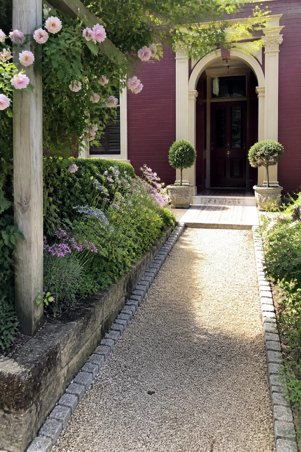 Gravel path to purple house with white archway, flanked by roses and topiary plants.