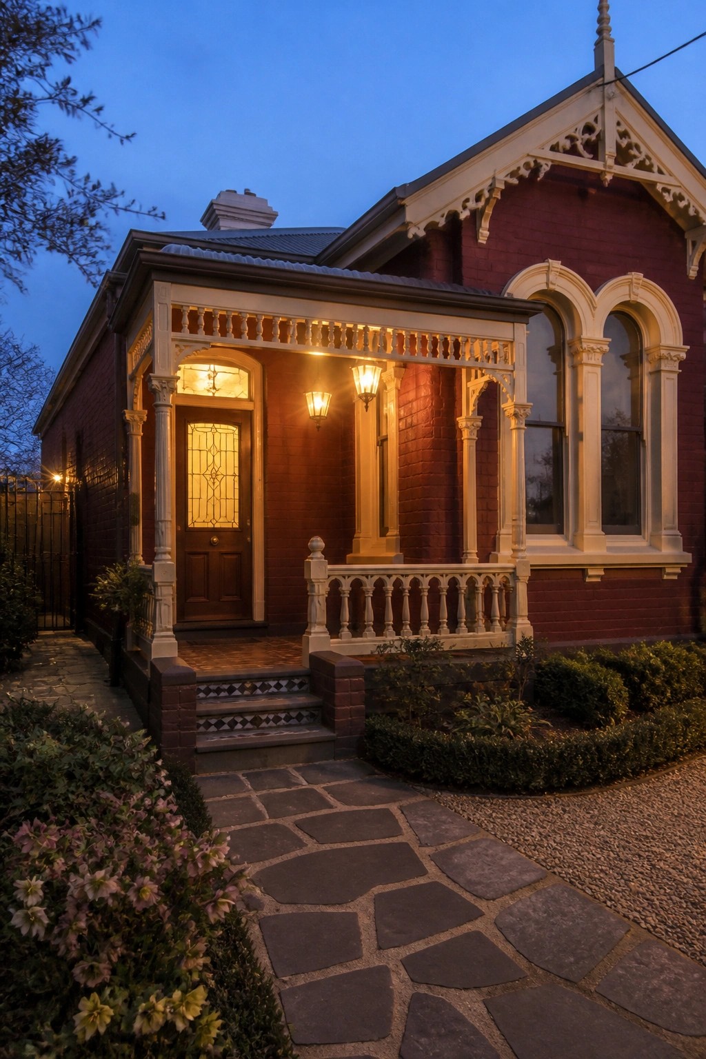 Red brick Victorian house with illuminated porch, arched windows, and stone path at dusk.