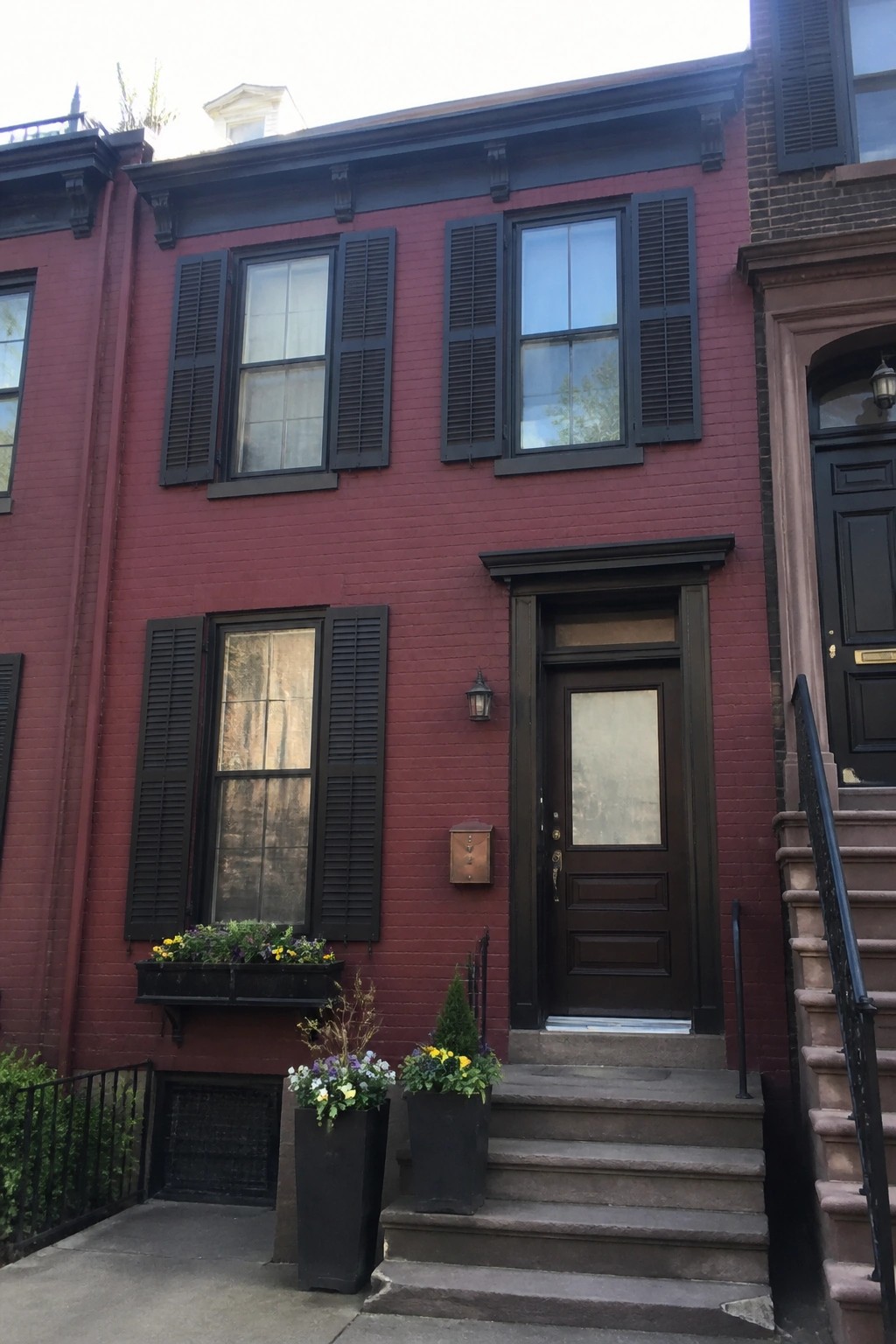 Red brick townhouse with black shutters, dark door, stone steps, and potted flowers.