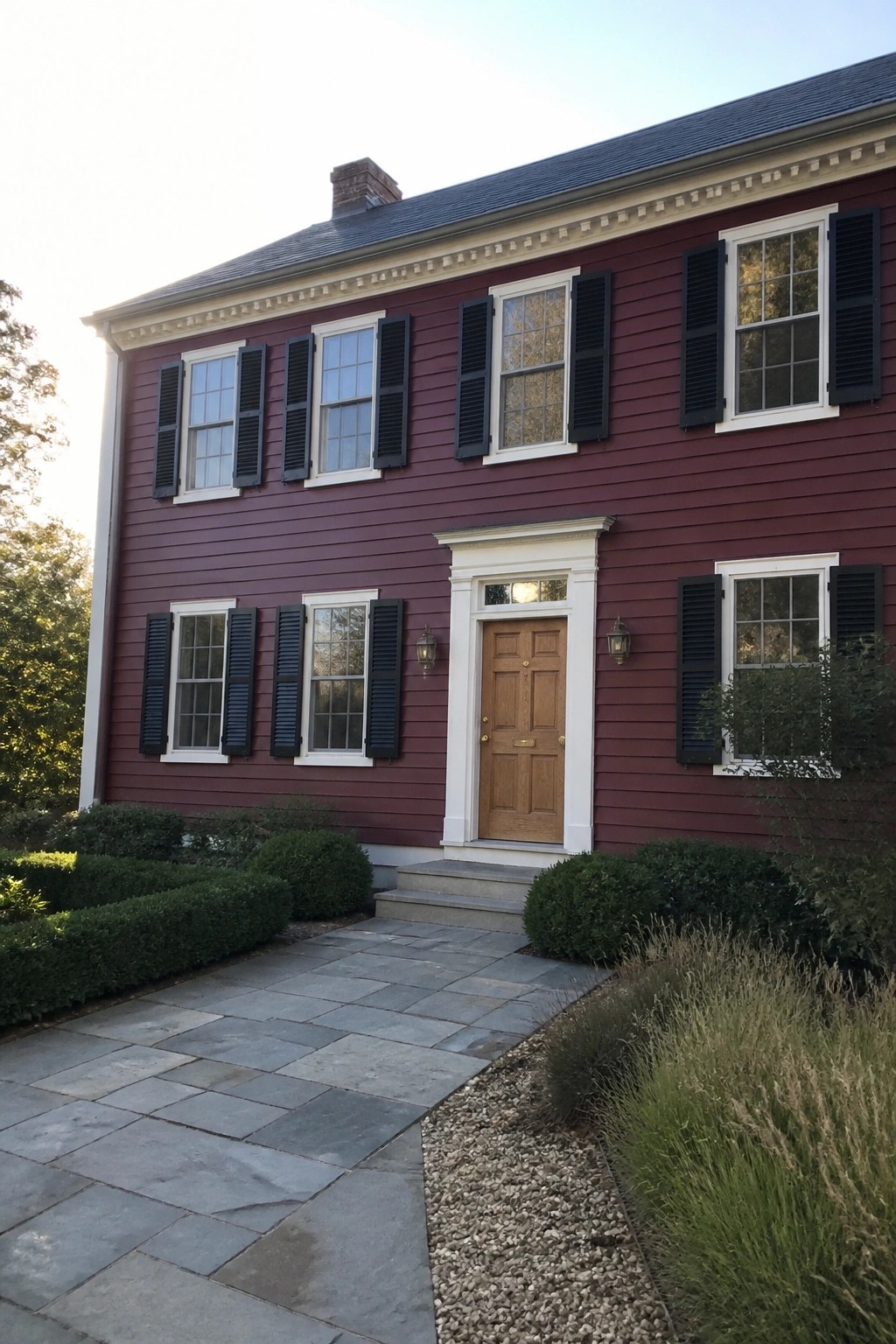 Red two-story house with black shutters, white trim, wooden door and stone path