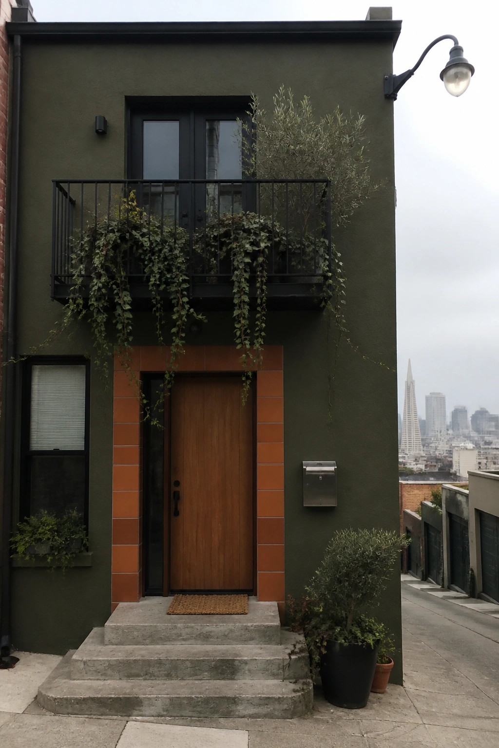 Olive-green modern home with wooden door, orange tiles, plant-filled balcony, and city skyline.