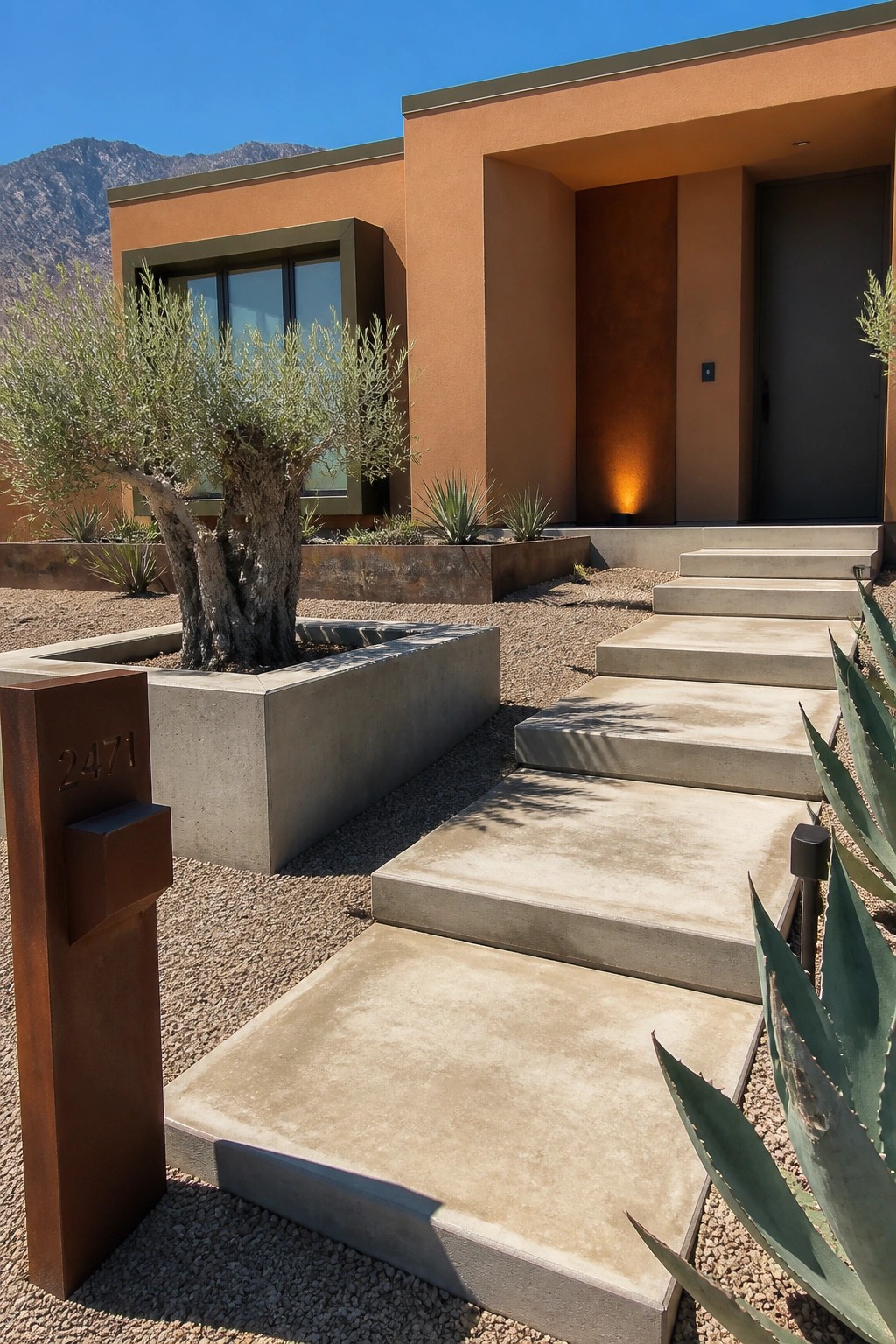 Modern orange house entrance with concrete steps, olive tree, agave plants, and address post 2471