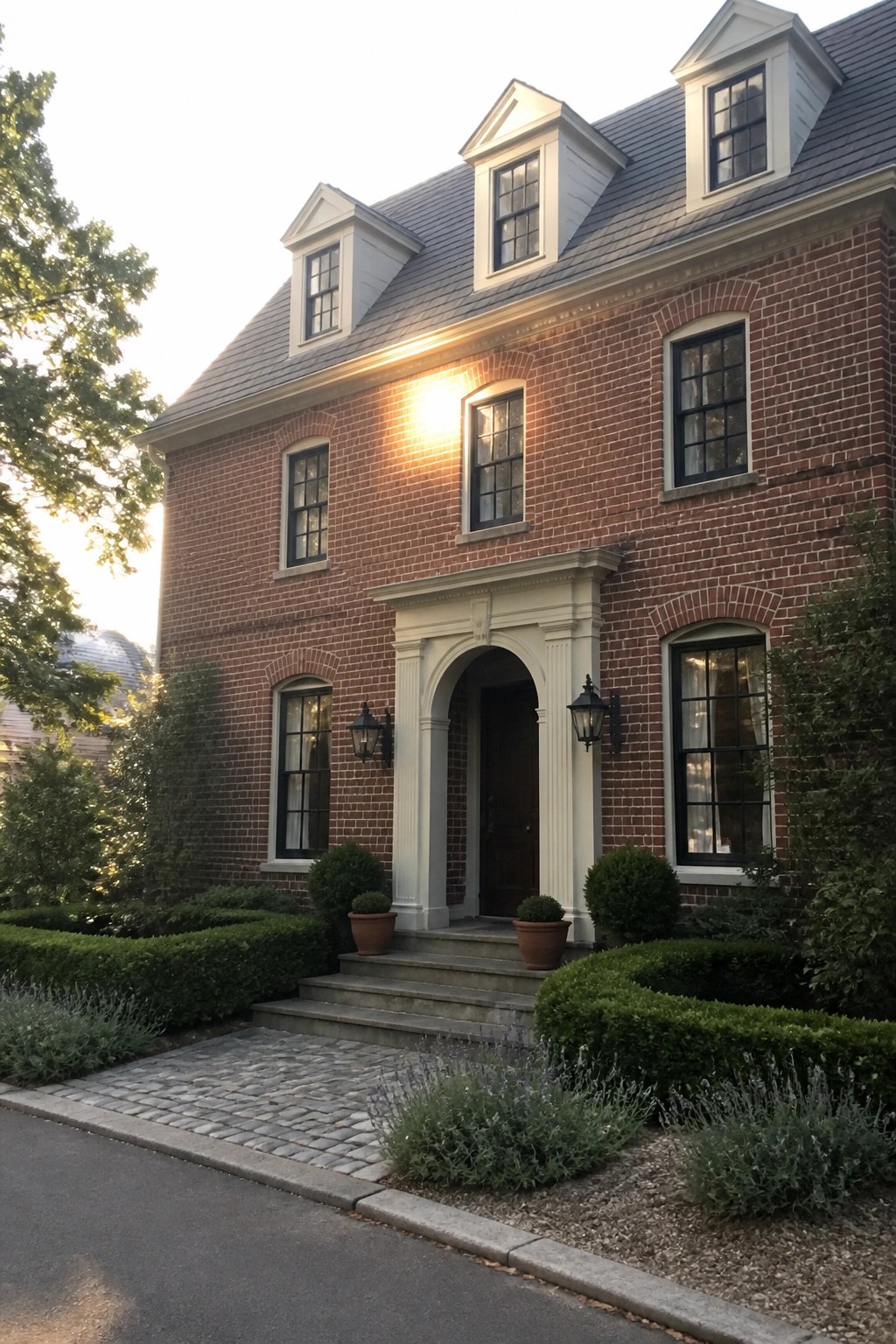 A two-story red brick house with white trim around the arched front entry, windows, and dormers, shown from the front with steps and landscaping.